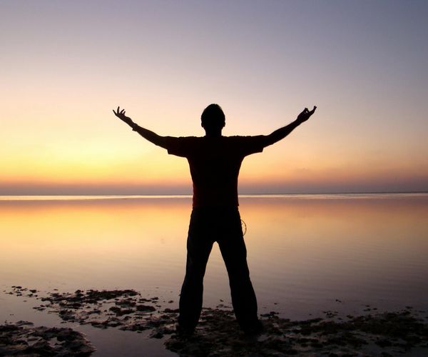 Silhouette of a person meditating at sunrise with a calm landscape.